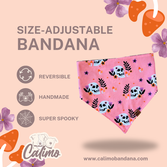 A pink reversible snap-on pet bandana with a pattern of skulls and flowers displayed against a floral background. The bandana has a caption that highlights its size-adjustable and handmade features.